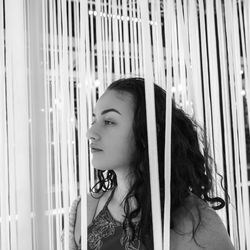 Close-up of thoughtful young woman standing amidst curtains