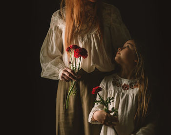 Midsection of mother and daughter holding flowers against black background