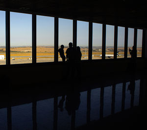 Silhouette people standing by railing against sky seen through window