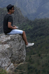 Side view of young man sitting on rock