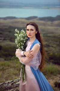 Woman stands on a mountain cliff in a blue long dress in summer