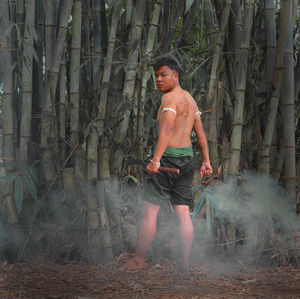 Portrait of shirtless young man standing by bamboo grooves in forest