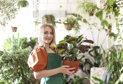 Young woman holding flower pot standing against plants