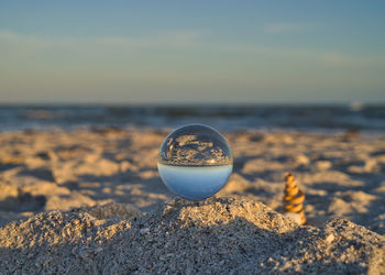 Close-up of crystal ball on rock at beach against sky