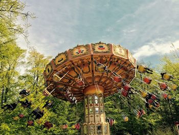 Low angle view of chain swing ride and trees against cloudy sky