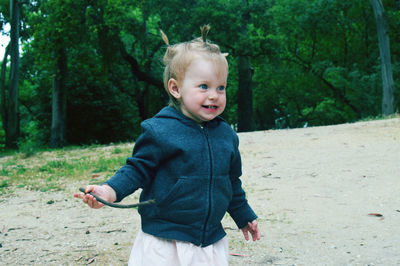 Baby girl holding stick while looking away against trees on field