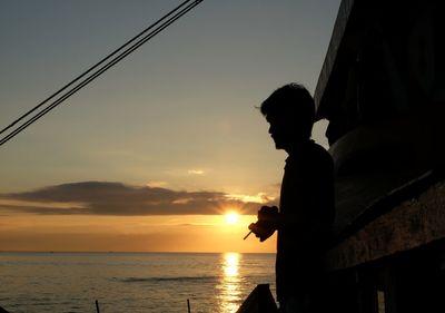 Silhouette man sitting by sea against sky during sunset