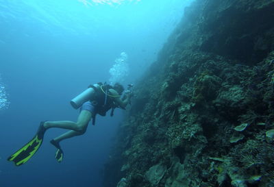 Low angle view of man scuba diving by coral in sea