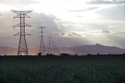 Electricity pylon on field against cloudy sky