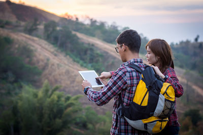 Rear view of couple holding mobile phone against sky during sunset