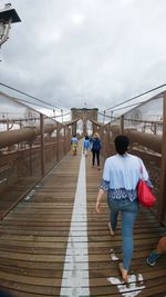 Rear view of people on footbridge against sky