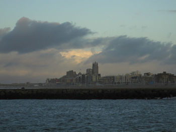 View of buildings by sea against cloudy sky