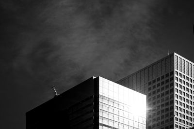 Monochrome low angle view of buildings reflecting the sun against sky