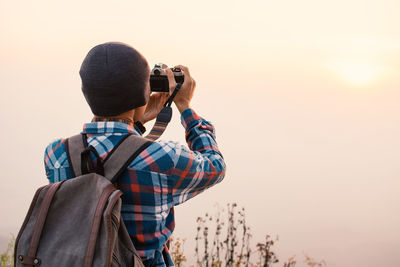 Rear view of backpacker photographing with camera against sky