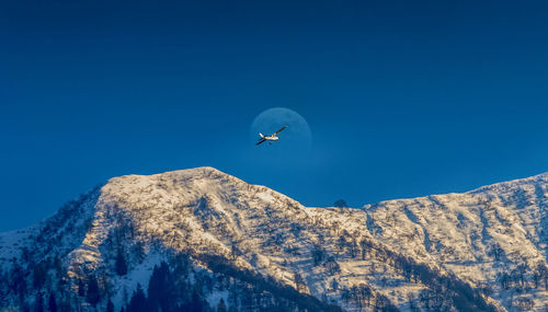 Low angle view of helicopter flying over snowcapped mountains against clear blue sky