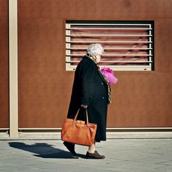 Woman holding umbrella while standing against wall