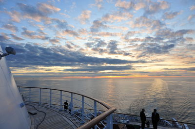 People standing in cruise ship on sea during sunset