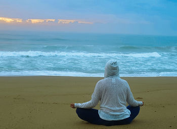 Rear view of man sitting on shore at beach against sky