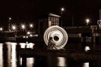 Side view of woman sitting on pier against wire wool over river