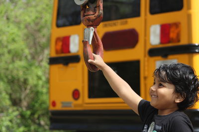 Playful boy smiling while holding metallic hook by bus