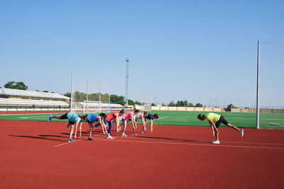 Group of women practice pre-workout stretching with their young traine