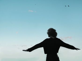 Rear view of woman with arms outstretched standing against sky