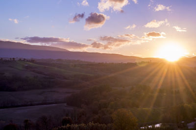 Sunlight streaming through clouds over landscape during sunset