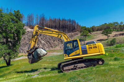 Mountainous terrain with excavator in foreground. large stone in bucket of excavator. 