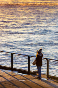 Rear view of woman standing on railing against sea