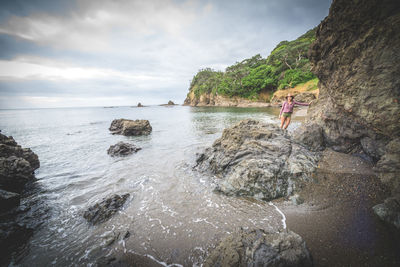 Woman standing on cliff by sea against sky