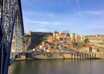 Bridge over river by buildings in city against sky