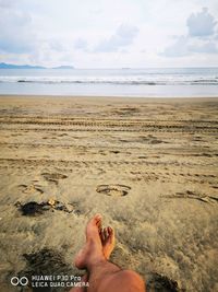 Low section of person on beach against sky