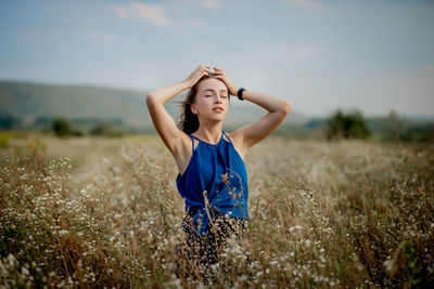 Young woman with arms raised standing on field against sky