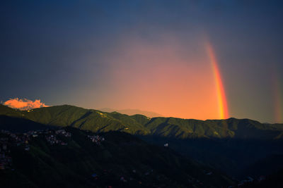 Scenic view of rainbow over mountains against sky during sunset