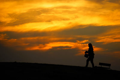 Silhouette woman walking on field against orange sky