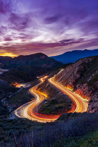 High angle view of light trails on winding mountain road against sky at sunset