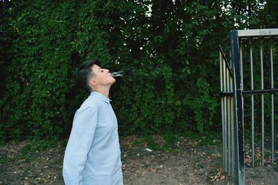 Side view of young man looking away against trees