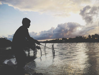 Silhouette man by lake against sky during sunset