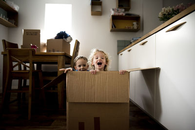 Portrait of cheerful siblings sitting in cardboard box at home