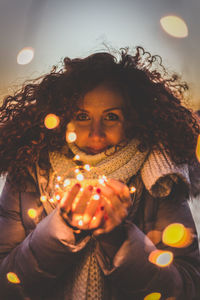 Portrait of young woman holding illuminated string lights in jar