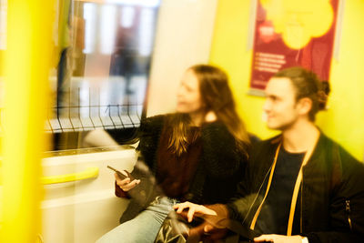 Smiling male and female friends sitting in train with reflection on glass door