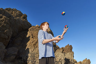 Boy juggling balls while playing against clear sky