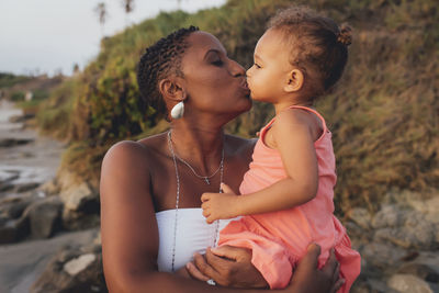 Mother kissing daughter while standing at beach