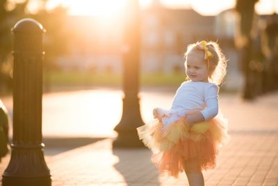 Cute girl wearing tutu standing on footpath at park during sunset