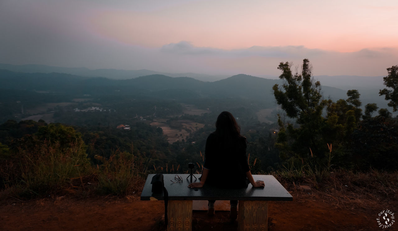 REAR VIEW OF MAN SITTING ON SEAT AGAINST MOUNTAIN