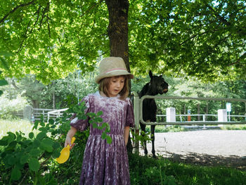 Portrait of small girl wearing lilac dress and summer hat and horse