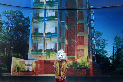 Man wearing mask while standing against residential building