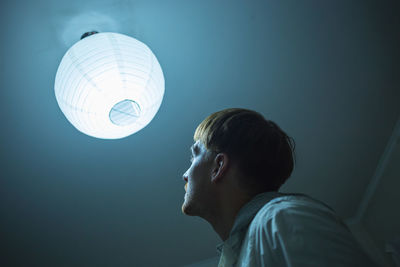 Low angle view of man looking at illuminated bulb at ceiling