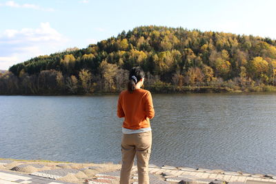 Rear view of woman standing by lake against sky