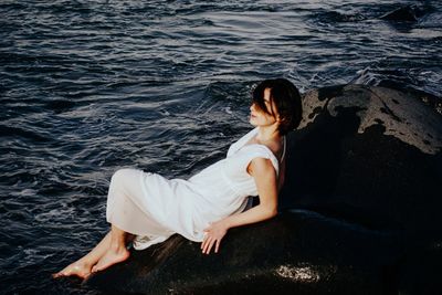 Side view of woman sitting on rock by sea